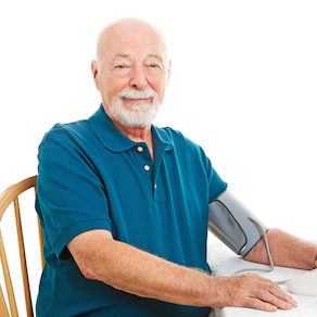 Senior man taking his blood pressure at home on the kitchen table.